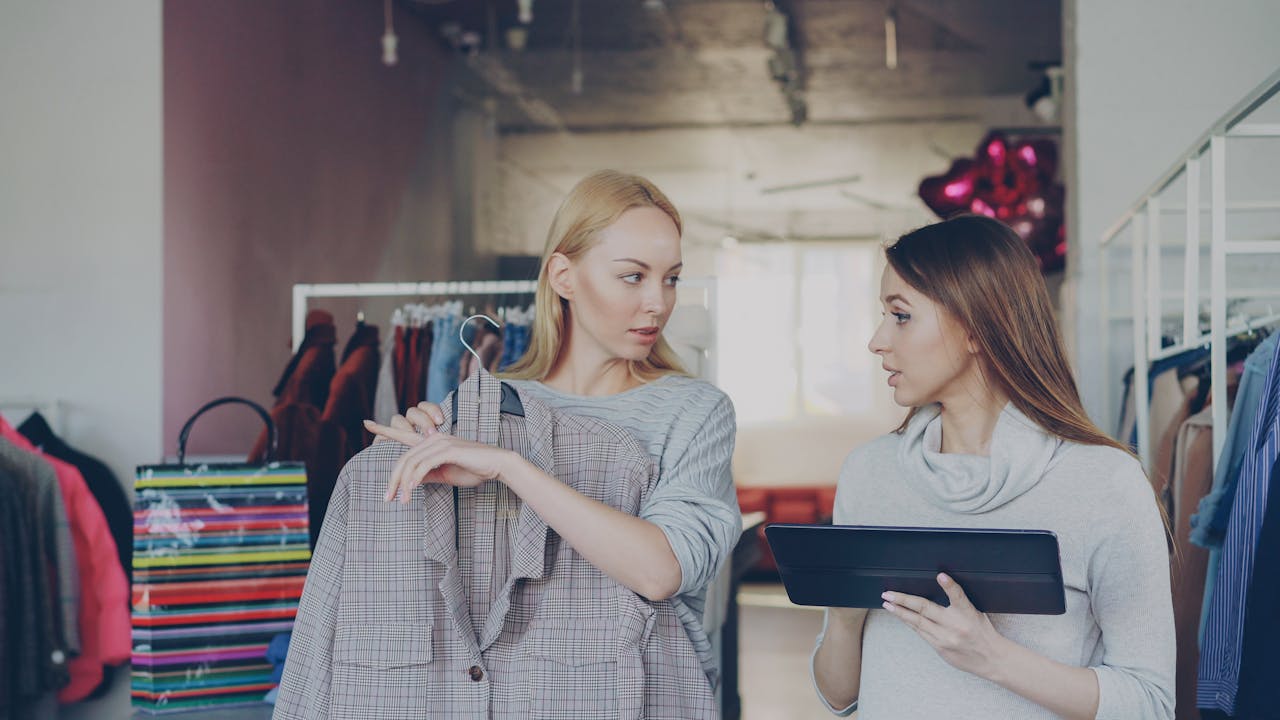 Two women in trendy boutique discussing clothing and style options, holding a plaid jacket.