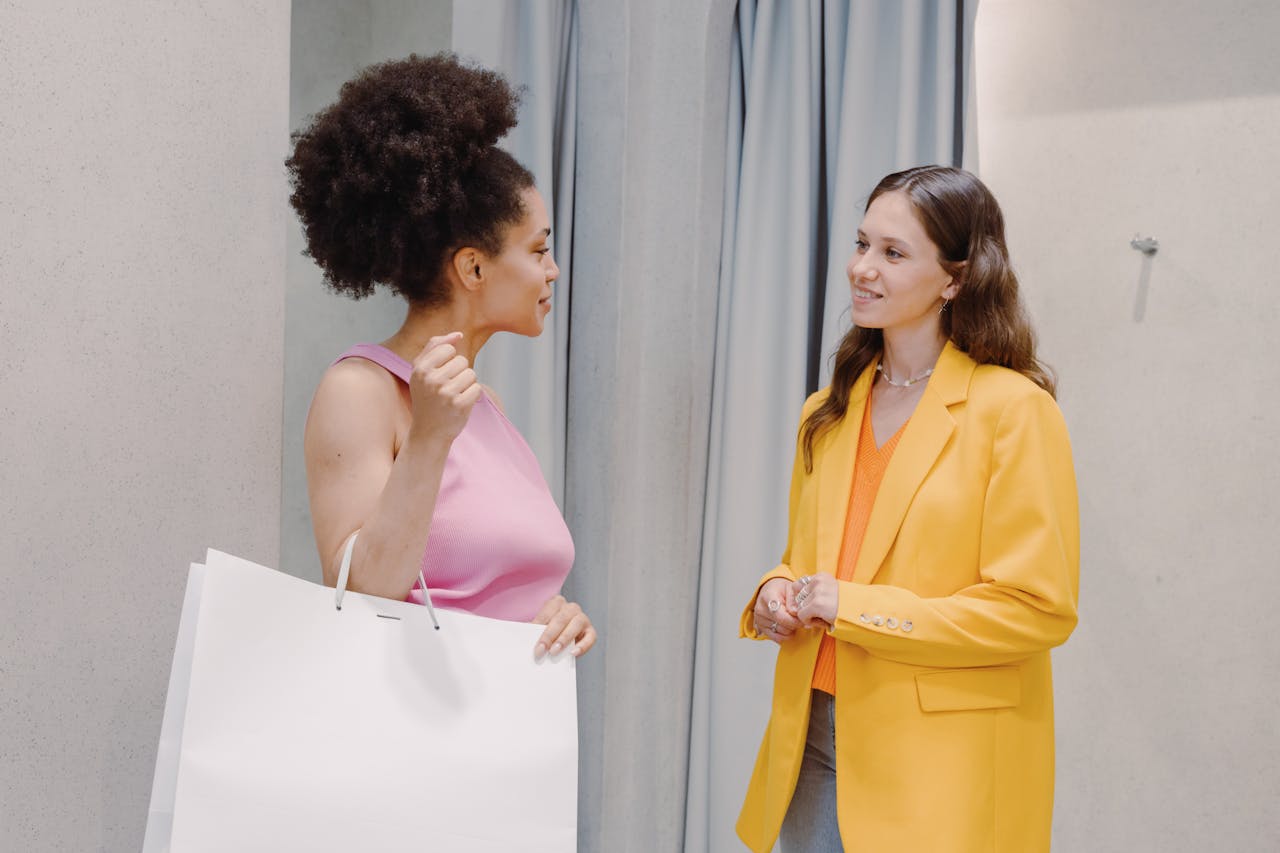 Two women discussing fashion and style in a clothing store setting, indoors.